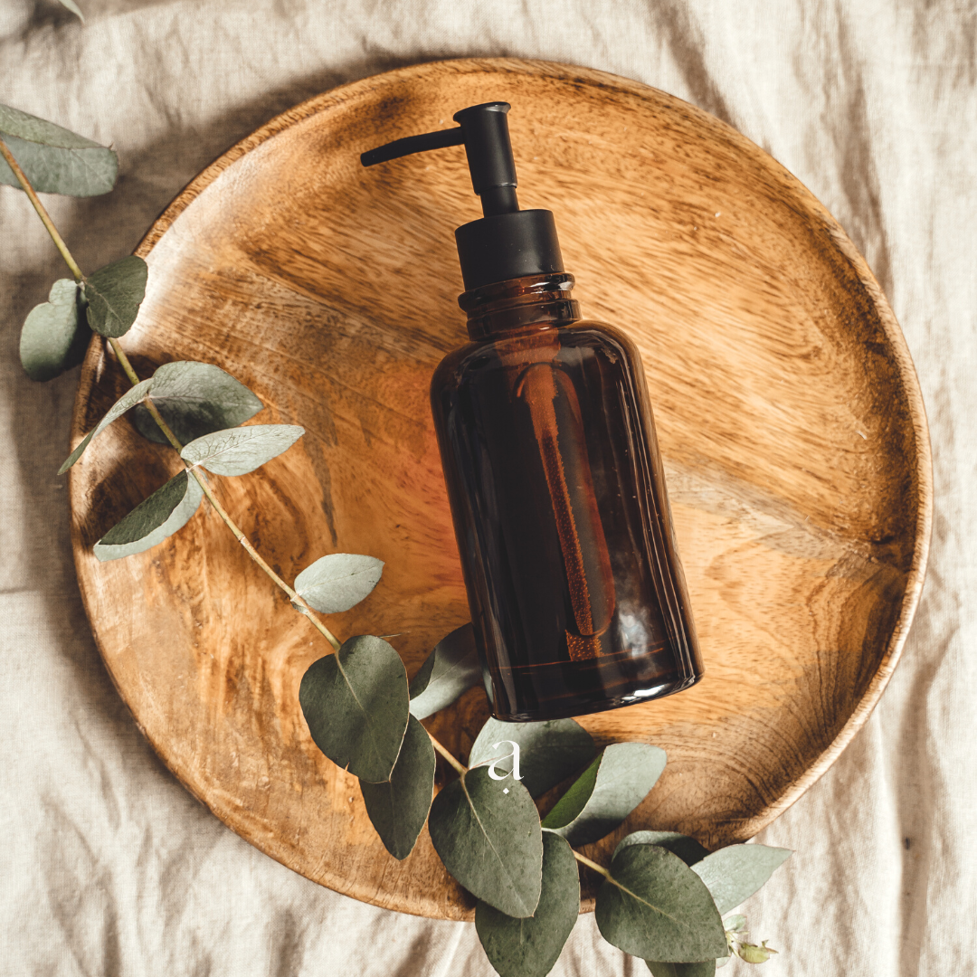 Sur un tissu en lin clair, un plateau en bois est visible au centre de l'image. Un spray diffuseur et une branche d'eucalyptus sont posés sur ce plateau.