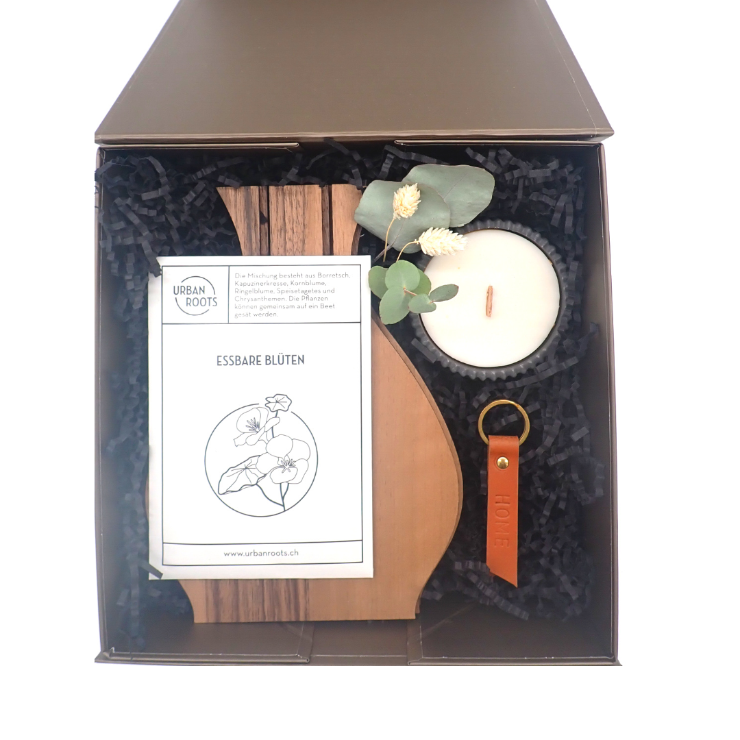 L'image représente le coffret aimanté ouvert. À l'intérieur, on peut y voir les produits listés dans la description du produit "Sunday at home". Les produits sont disposés sur du papier frizz de couleur foncée. Un petit bouquet de fleurs séchées agrémente le coffret.