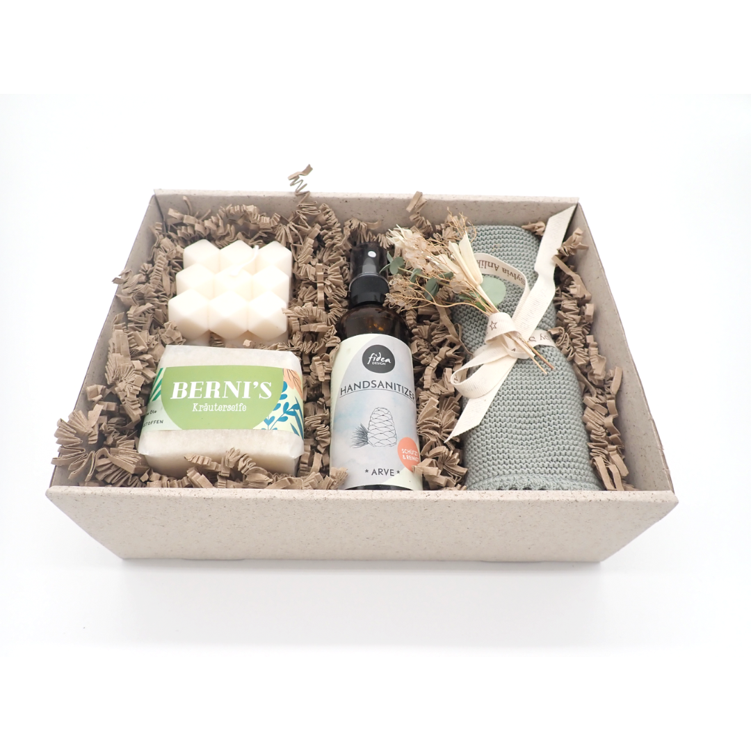 L'image représente le coffret de papier d'herbe ouvert (sans couvercle). À l'intérieur, on peut y voir les produits listés dans la description du produit "Welcome Home". Un petit bouquet de fleurs séchées agrémente le coffret. Les produits sont disposés sur du papier frizz de couleur claire.