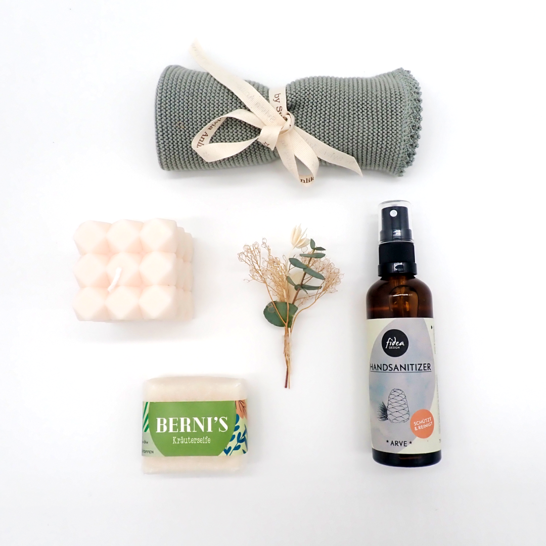 Les produits du coffret "Welcome Home" sont disposés à plat, en forme de cercle. Un petit bouquet de fleurs séchées est posé au centre de l'image.