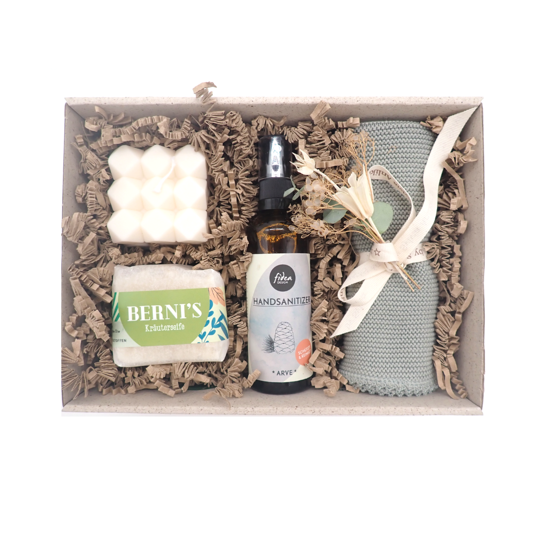 L'image représente le coffret de papier d'herbe ouvert (sans couvercle). À l'intérieur, on peut y voir les produits listés dans la description du produit "Welcome Home". Un petit bouquet de fleurs séchées agrémente le coffret. Les produits sont disposés sur du papier frizz de couleur claire.