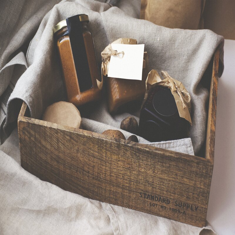 L'image représente une boîte en bois avec des pots de confitures à l'intérieur, posés sur un tissu en lin. Cette image sympbolise les valeurs "Originalité et empreinte locale".